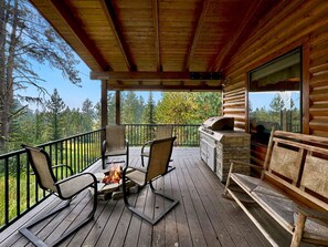 Una terraza de madera con mobiliario exterior, una chimenea de piedra y una parrilla de piedra.