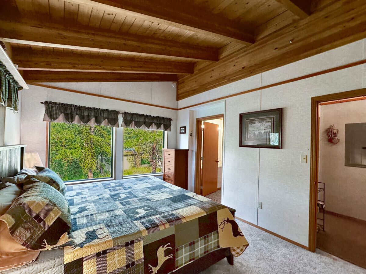 Ein Schlafzimmer mit einem großen Bett, einem Fenster mit Blick auf Bäume, einer Tür und einem gerahmten Bild an der Wand.