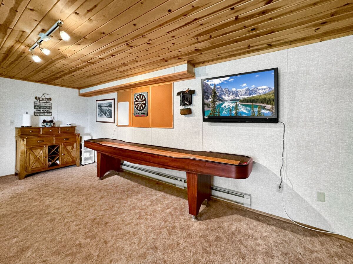 A room with a dartboard, a pool table, a wooden cabinet, and a framed picture of a mountain landscape.