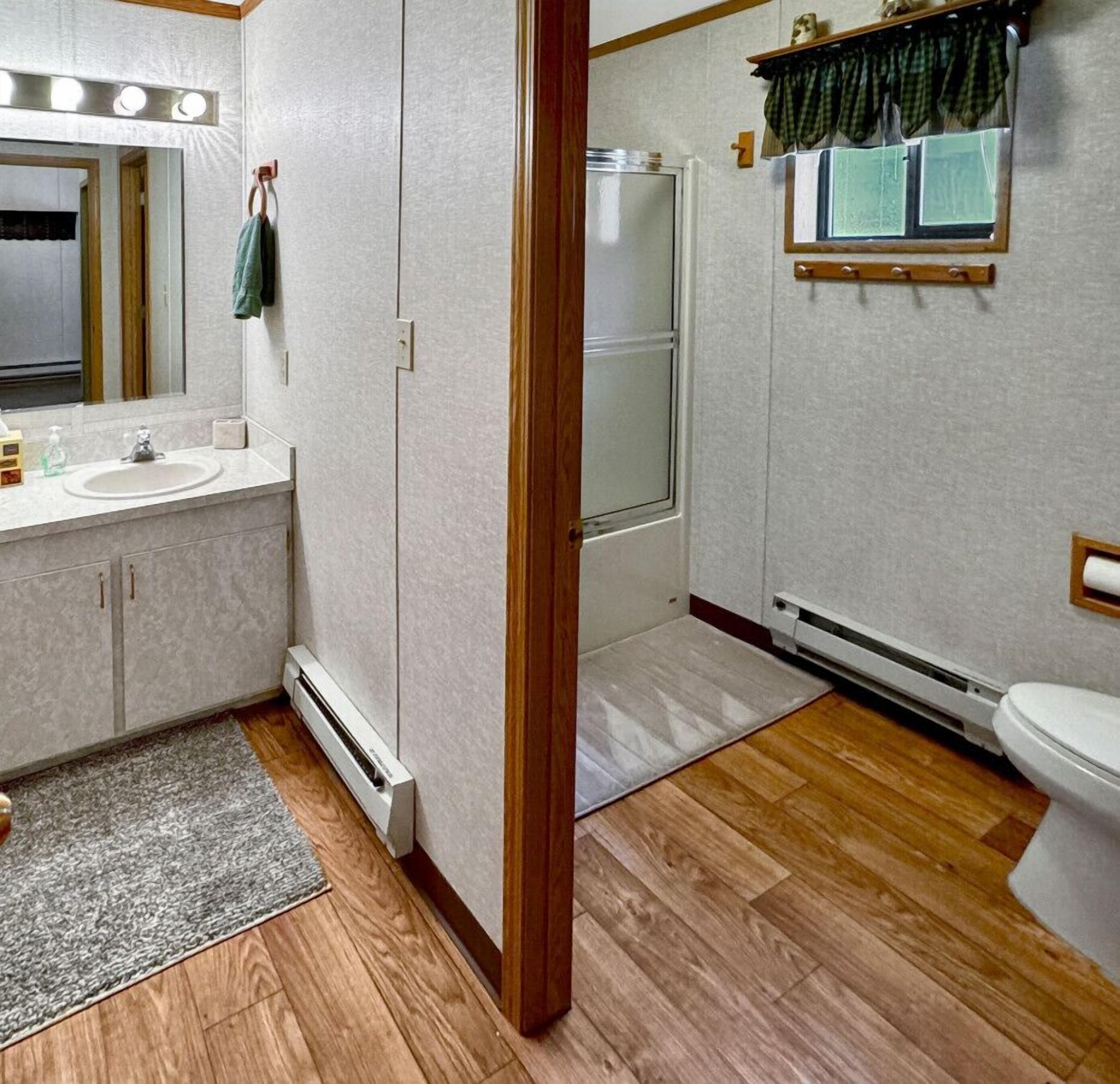 A bathroom with a sink, mirror, towel rack, shower, and toilet.