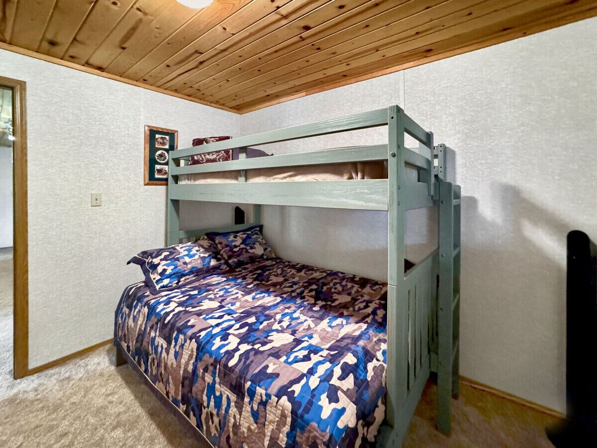 Una litera con colcha de estampado camuflado en una habitación con techo y paredes de madera.
