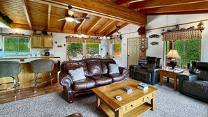 A cozy living room with a leather sofa, wooden coffee table, and a dining area with a bar. - Rustic Cabin with Modern Comforts! (Cascade)