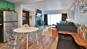 Un salon moderne avec un canapé gris, une table basse en bois et un coin repas comprenant une table blanche et des chaises transparentes.