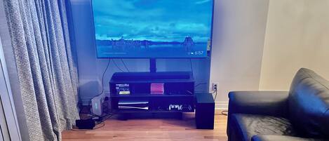 Una sala de estar con un televisor de pantalla plana sobre un mueble bajo, un sofá de cuero y piso de madera.