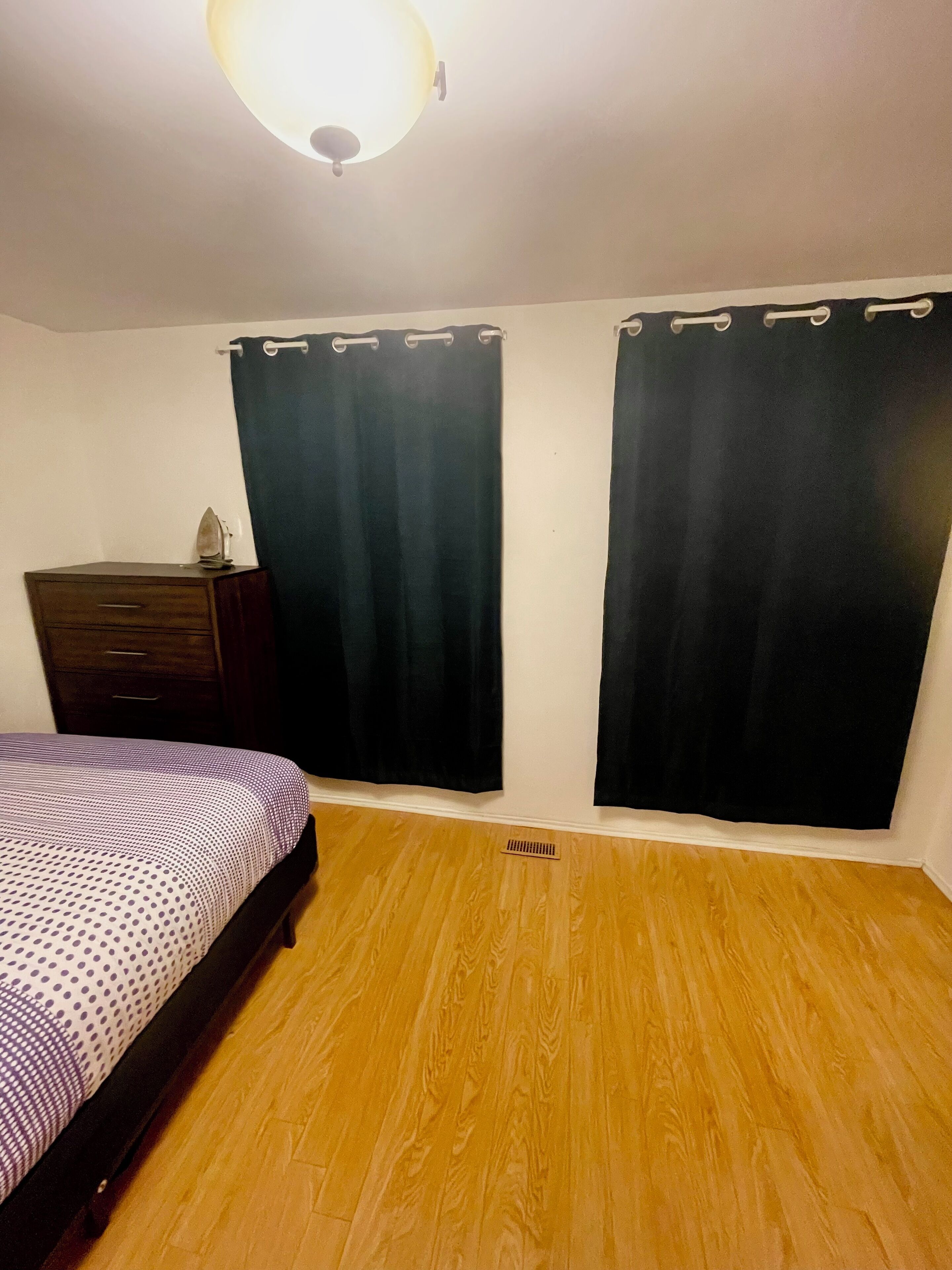 Une chambre à coucher avec un lit, une commode et deux rideaux.