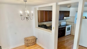 Cocina con armarios de madera, estufa y microondas. Hay una cesta de mimbre y una araña.