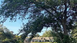 A serene lakeside view with a house in the background, surrounded by lush greenery and a calm water body reflecting the trees. - Tranquil Lake view 2 Bedroom 2 bath Villa in Myrtle Trace (Venice)