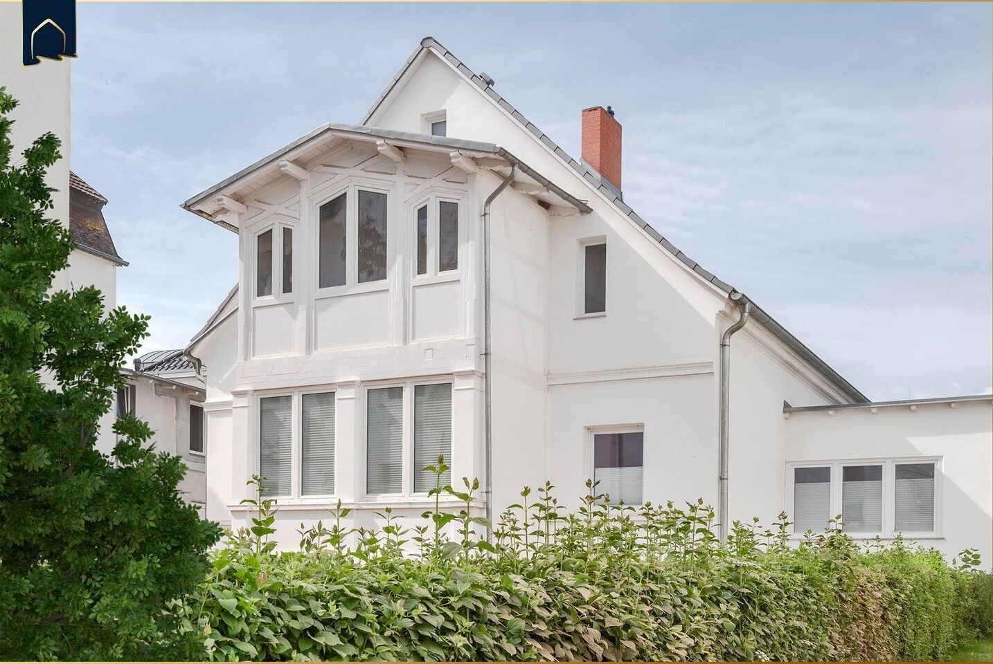 Ein weißes, zweistöckiges Haus mit Satteldach, mehreren Fenstern und einem sichtbaren Schornstein.