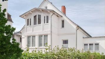 Ein weißes, zweistöckiges Haus mit Satteldach, mehreren Fenstern und einem sichtbaren Schornstein.