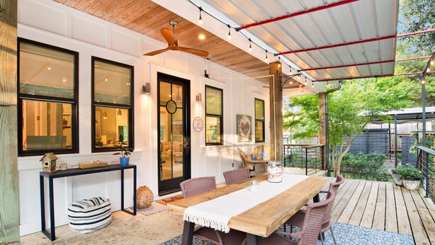 A covered patio area with a wooden table and chairs, a ceiling fan, and a view of the garden.