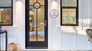 A modern building entrance with a black door, a "Love Cottage" sign, and a wicker chair outside.