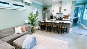A modern kitchen with a central island, dining chairs, and a sofa in a living area.