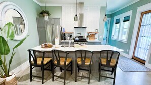 A modern kitchen with a central island, four chairs, a large mirror, and a potted plant.