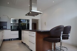 A modern kitchen with a central island, stainless steel appliances, and two bar stools.