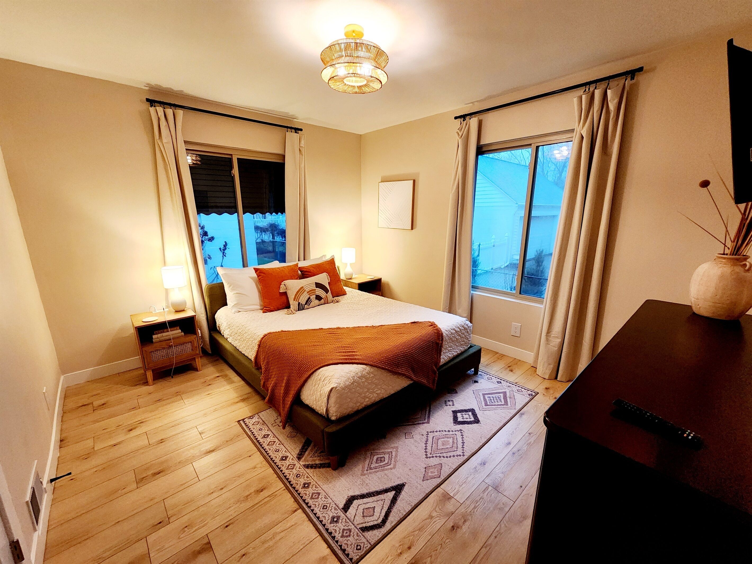 Une chambre à coucher comprenant un lit, des tables de chevet, une lampe, un téléviseur, une fenêtre et une vue sur l’extérieur.