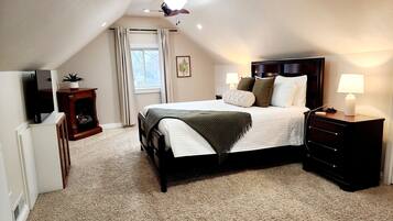 A bedroom with a bed, bedside lamps, a nightstand, a TV, a fireplace, and a ceiling fan.