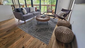 Ein modernes Wohnzimmer mit grauem Sofa, einem Holztisch und einem großen Fenster mit Blick auf Grünflächen.