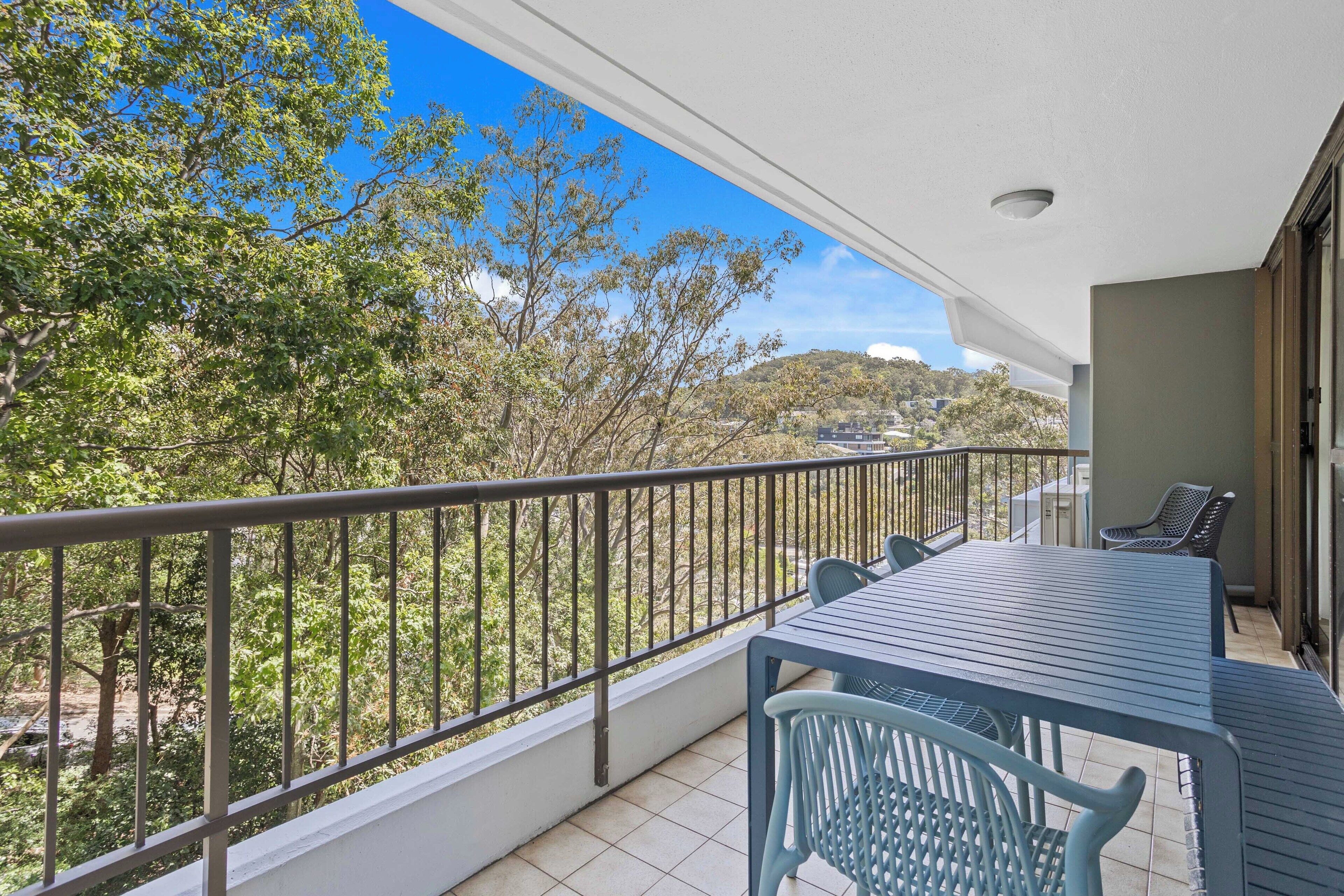 A balcony with a table and chairs, a railing, and a view of trees and buildings.