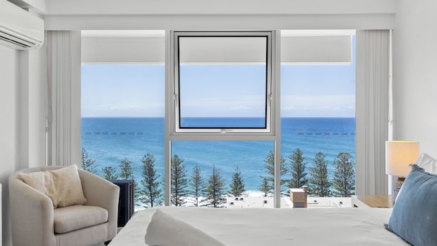 A hotel room with a large window offering a view of the sea and trees. - Burleigh Headland 2 Bedroom Stay, just a stones throw from the beach! (Burleigh Heads)