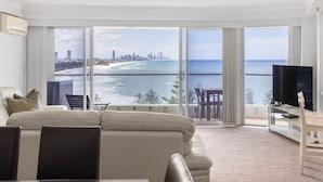 A modern hotel room with a large balcony, a sofa, a TV, and a dining area with a view of the ocean and city skyline. - Burleigh Headland 2 Bedroom Stay, just a stones throw from the beach! (Burleigh Heads)