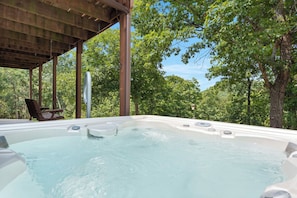 Un jacuzzi bajo una pérgola de madera rodeado de árboles.