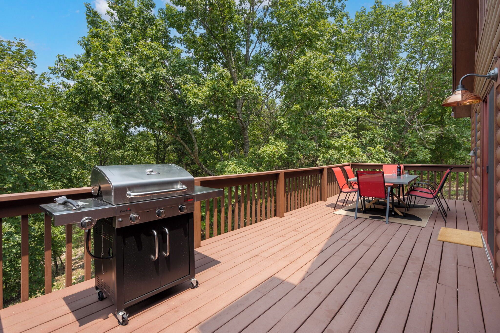 Una terraza al aire libre con una parrilla, una mesa con sillas y vistas a árboles.