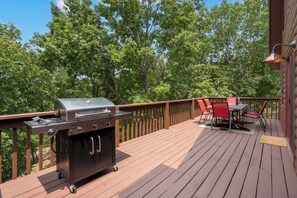 Une terrasse extérieure avec un barbecue, une table et des chaises, et une vue sur les arbres.