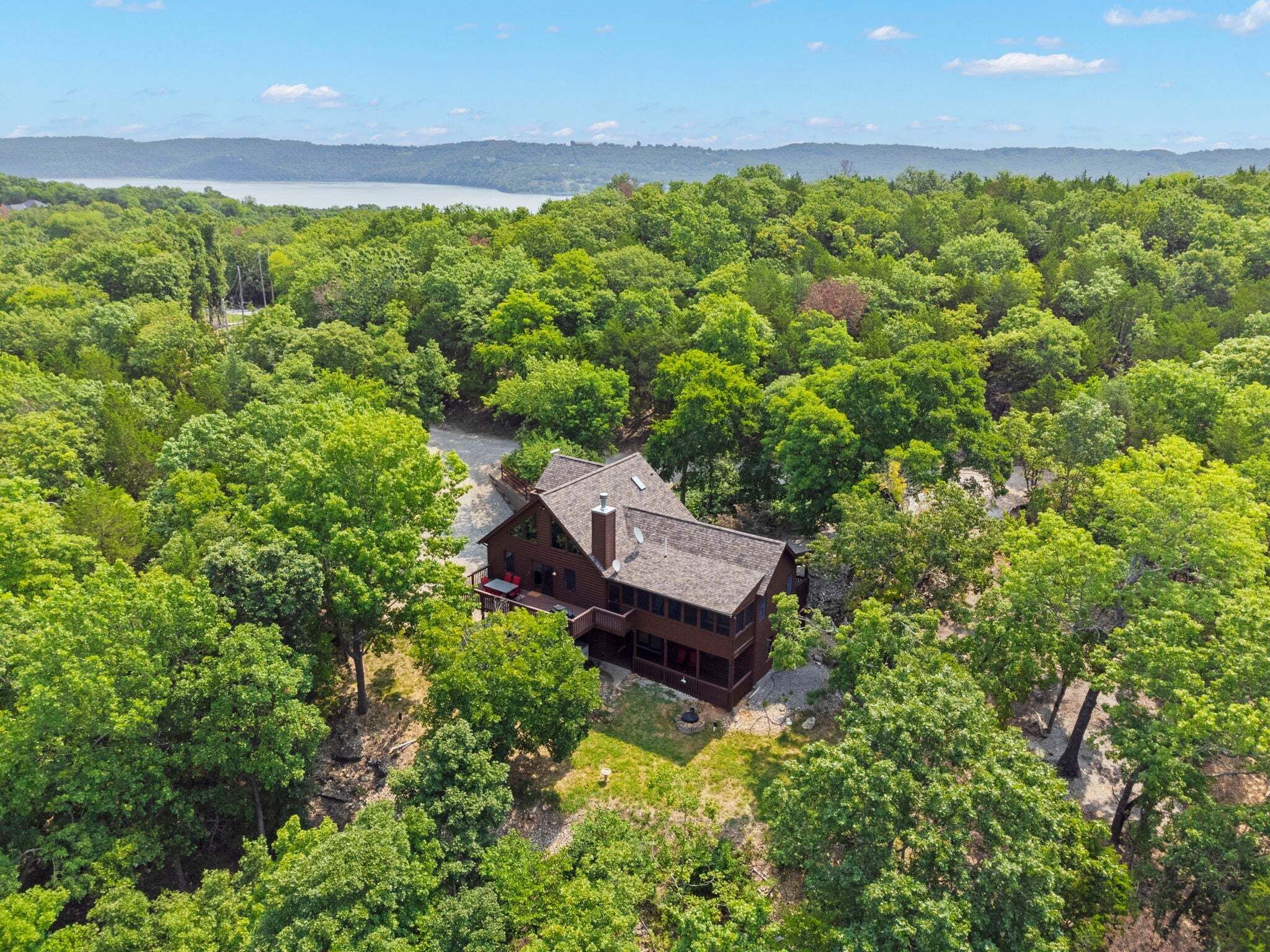 A two-story cabin surrounded by dense forest, with a clear view of the lake and mountains in the distance.