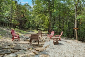 A forested area with a gravel path, red Adirondack chairs, a wooden bench, and a sign indicating a trail to a lake.