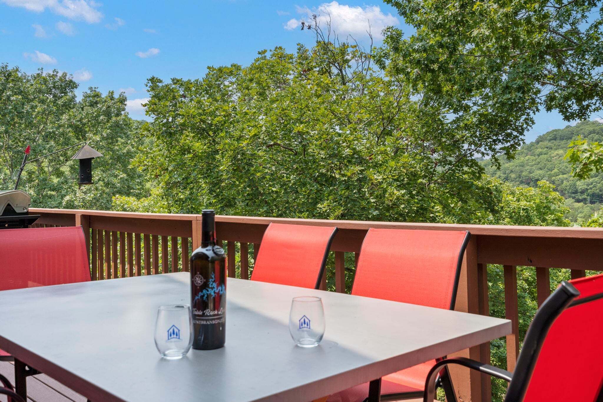 An outdoor dining area with a table, chairs, a bottle, and glasses.