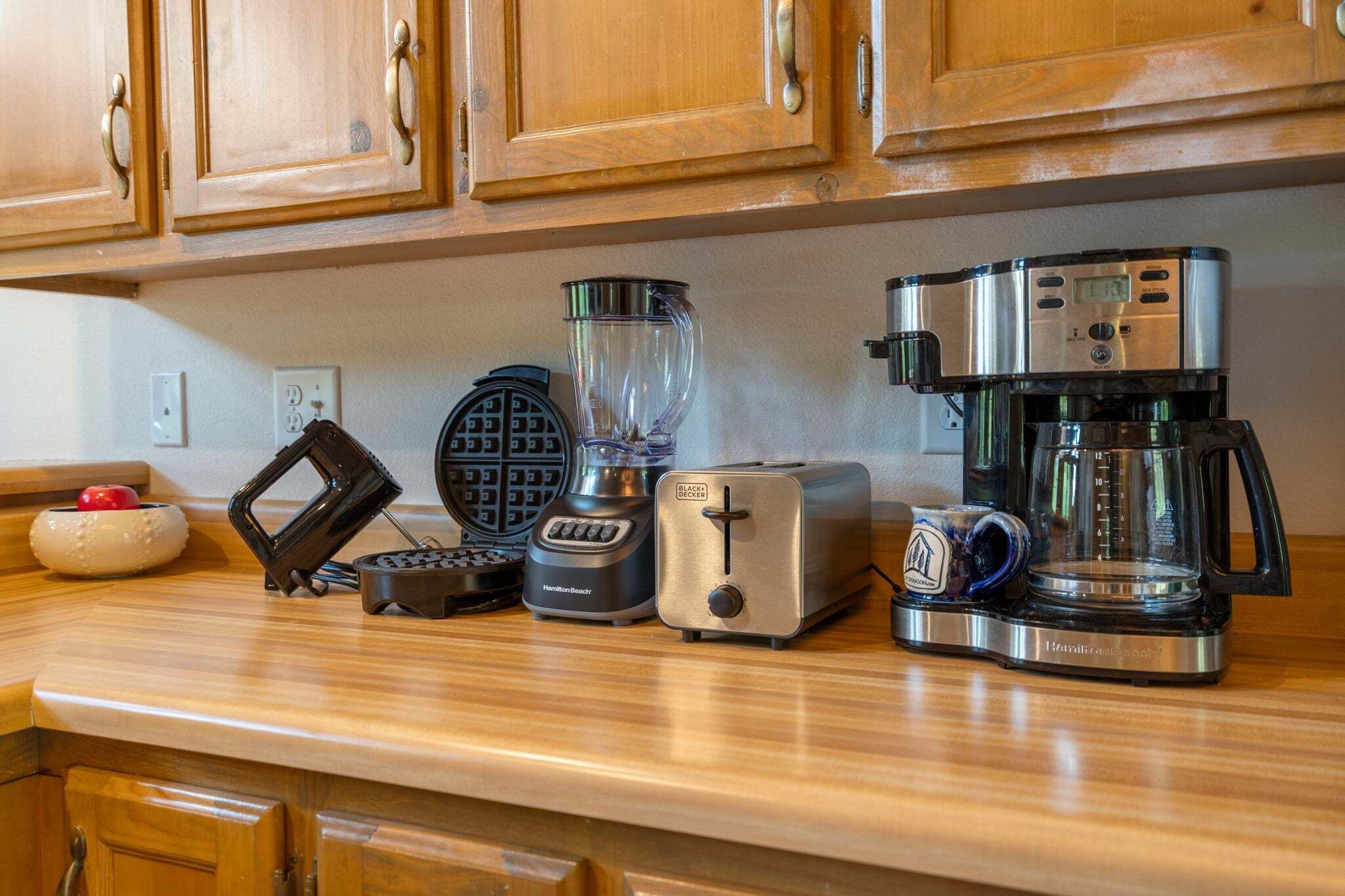 A kitchen counter with a waffle maker, blender, toaster, and coffee maker.