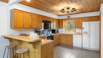 A kitchen with wooden cabinets, a central island with stools, a microwave, stove, and a refrigerator.