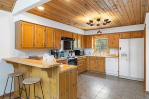 Une cuisine avec des meubles en bois, un îlot central doté de tabourets, un four à micro-ondes, une cuisinière et un réfrigérateur.