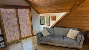 A cozy living room with a grey sofa, a patterned rug, wooden flooring, and a sloped ceiling. - Private 4.5-Acre Retreat featuring Hot Tub-Firepit-Walk to Table Rock-Free Daily Attraction Tickets (Lampe)