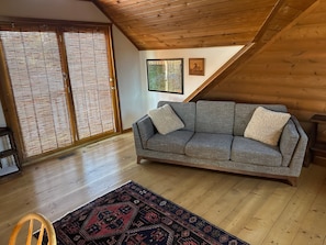 Una sala de estar acogedora con un sofá gris, un tapete estampado, piso de madera y techo inclinado.