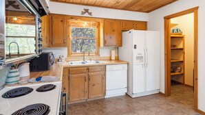 A compact kitchen with wooden cabinets, a white refrigerator, a stove, and a sink. - Private 4.5-Acre Retreat featuring Hot Tub-Firepit-Walk to Table Rock-Free Daily Attraction Tickets (Lampe)