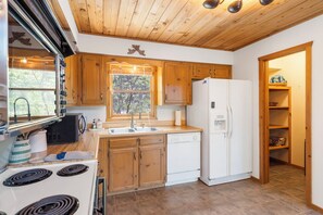 Une cuisine de taille réduite, avec des meubles de rangement en bois, un réfrigérateur blanc, une cuisinière et un évier.