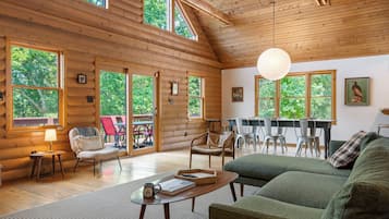 Ein geräumiges Blockhaus-Interieur mit mehreren Sitzbereichen, großen Fenstern und einer hohen Decke.