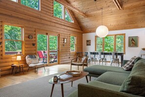 Ein geräumiges Blockhaus-Interieur mit mehreren Sitzbereichen, großen Fenstern und einer hohen Decke.