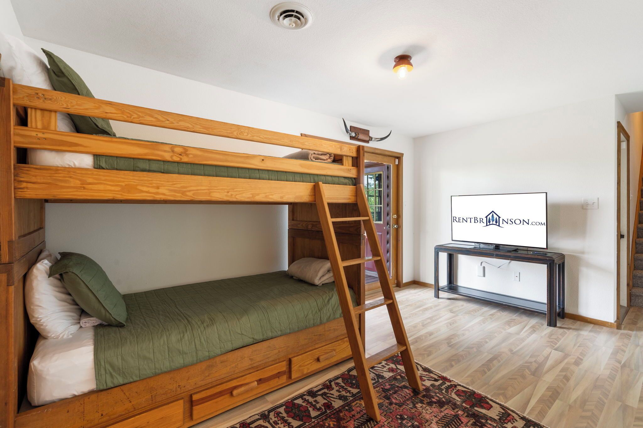 Una cama litera con escalera, un televisor y una alfombra estampada en una habitación con suelo de madera.