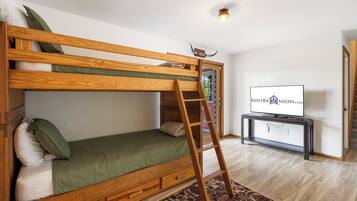 Una cama litera con escalera, un televisor y una alfombra estampada en una habitación con suelo de madera.