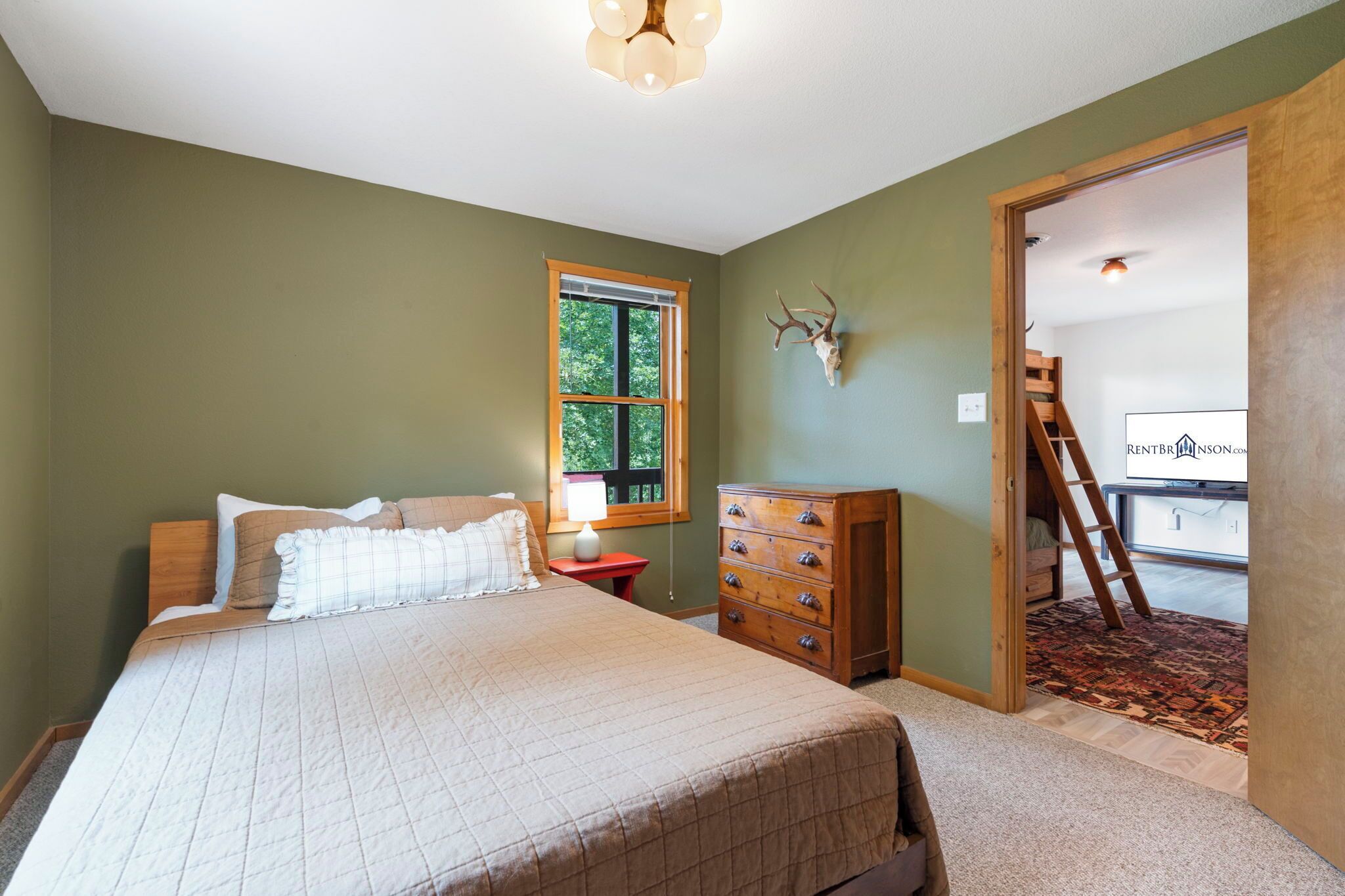 A bedroom with a bed, dresser, window, and a door leading to another room.