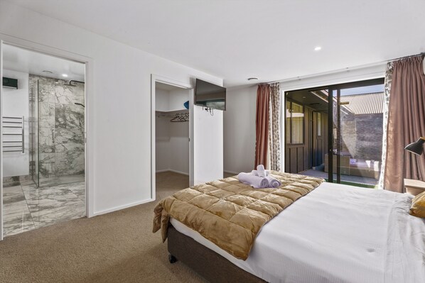 A hotel room with a bed, a walk-in closet, a bathroom with a glass shower, and a view of the outside.