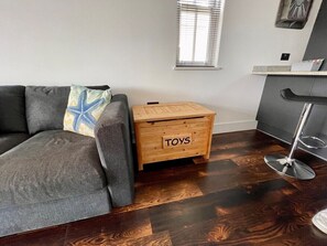 A living room with a gray sofa, a wooden side table labeled "TOYS," and a wooden floor. - HipNautic, Mevagissey, sleeps 6 (Mevagissey)