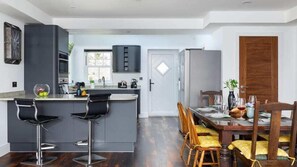 A modern kitchen with a central island, bar stools, a dining table with chairs, and a refrigerator. - HipNautic, Mevagissey, sleeps 6 (Mevagissey)