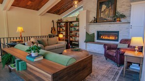 Una sala de estar acogedora con chimenea, techo de madera y una estantería llena de libros.