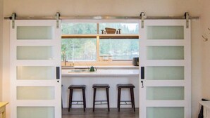 Una habitación con cama, una zona de cocina con taburetes y una puerta corrediza con paneles de vidrio esmerilado.