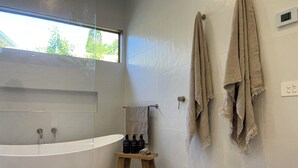 A modern bathroom with a freestanding bathtub, a small wooden stool with toiletries, and two towels hanging on a wall-mounted rack.