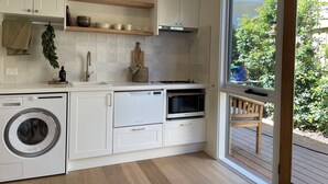A modern kitchen with white cabinets, a built-in washing machine, a stove, and a large window offering a view of the outdoors.