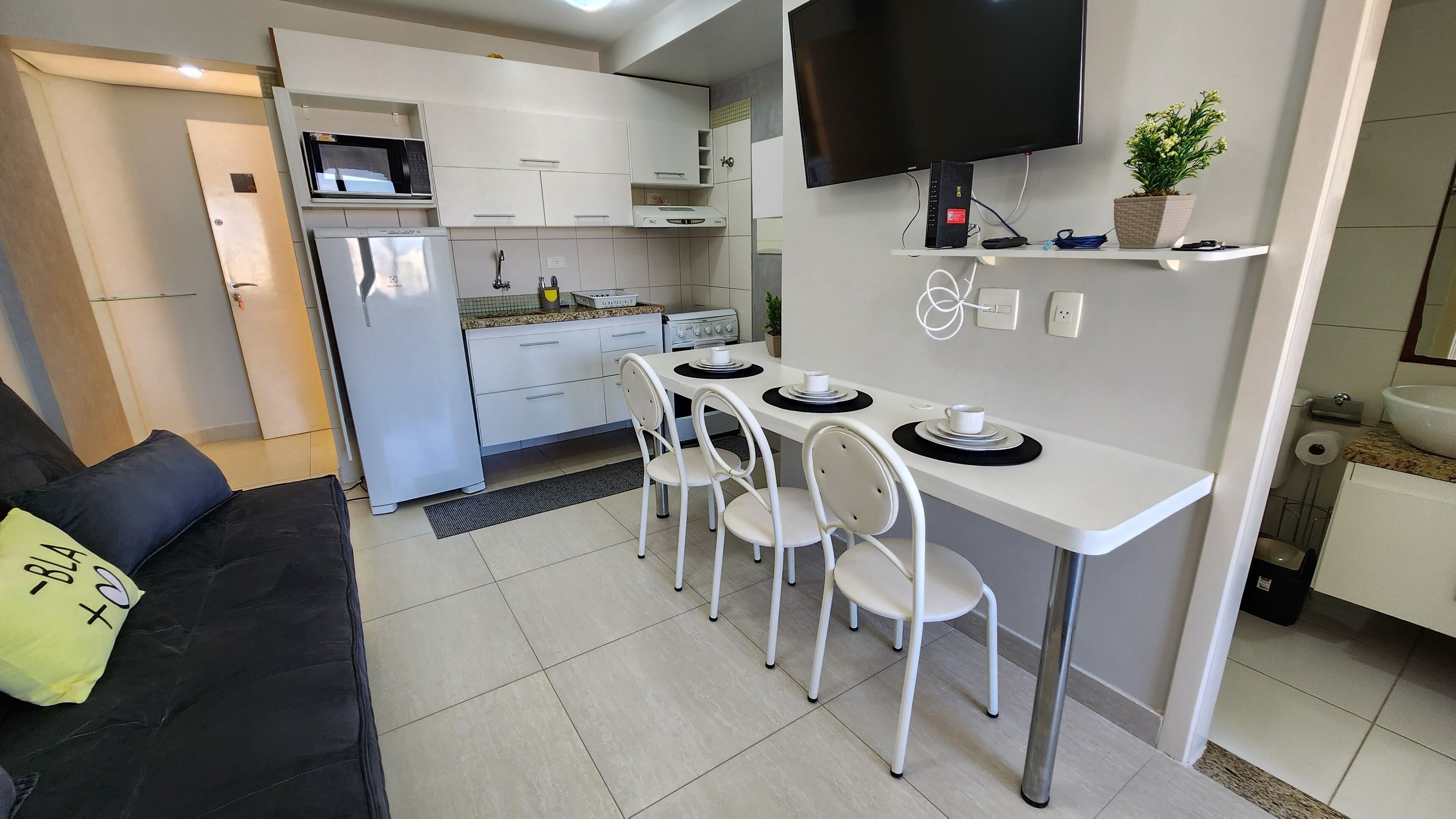 A modern kitchen with white cabinets, a built-in microwave, a stove, and a dining area with white chairs and a small table.